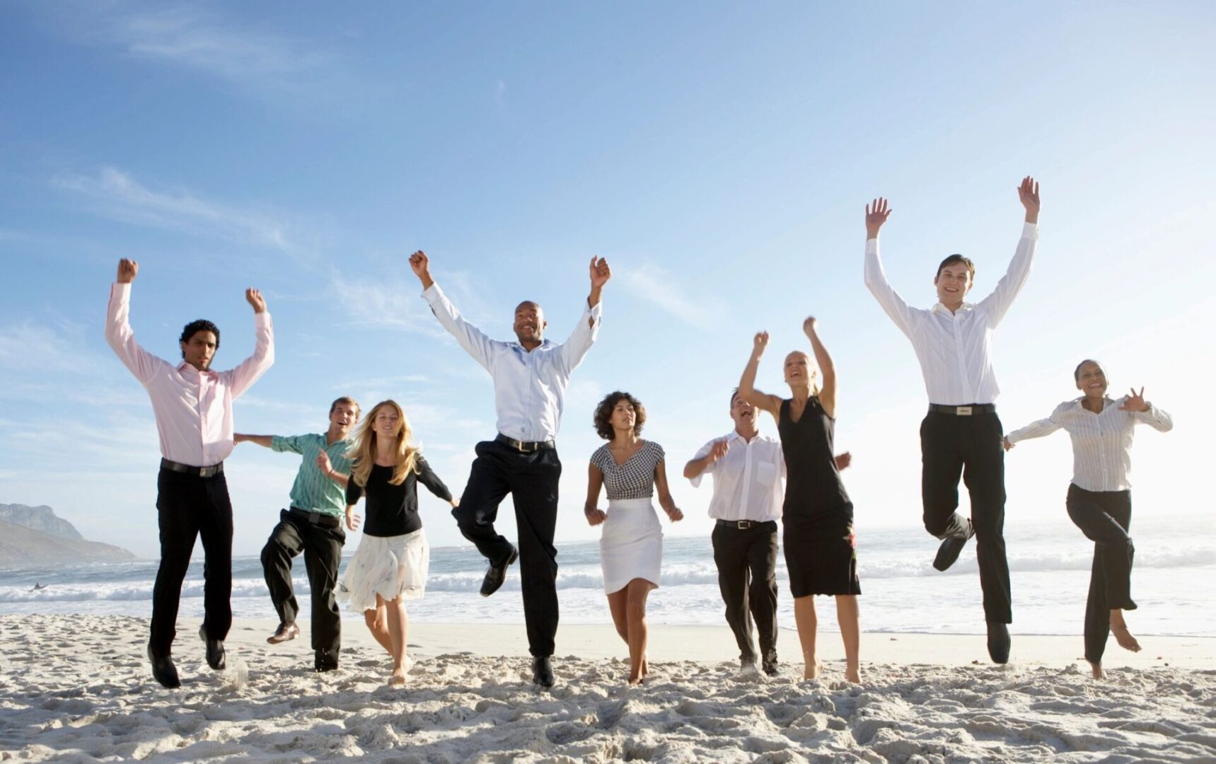 A group of people jumping up in the air on a beach.