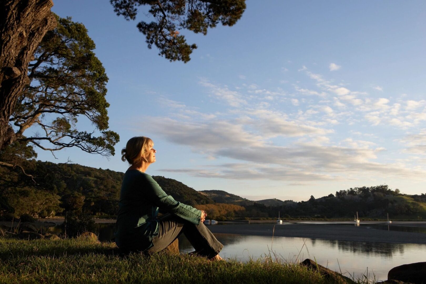 A woman sitting on the grass near a body of water.