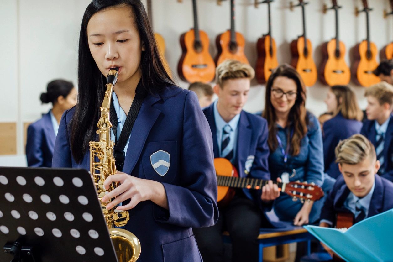 A group of students playing instruments in front of guitars.